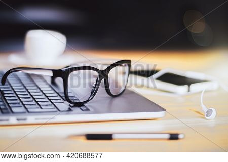 Stylish Glasses On Laptop Keyboard With Headphones Connceted To Modern Smartphone On Wooden Surface