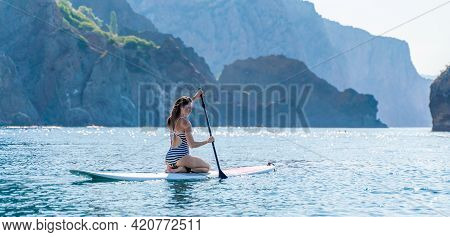 Banner. Sporty Girl On A Glanders Surfboard In The Sea On A Sunny Summer Day. In A Striped Swimsuit,
