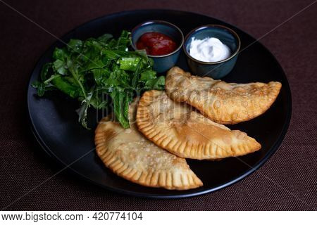 Appetizing Fried Chebureks On A Black Plate With Greens