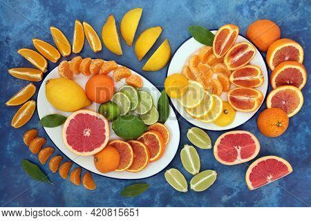 Citrus fruit to boost the immune system with oranges, lemons, limes and grapefruit on plates. High in antioxidants, anthocyanins, lycopene, fibre and vitamin c. Health care concept. On mottled blue.
