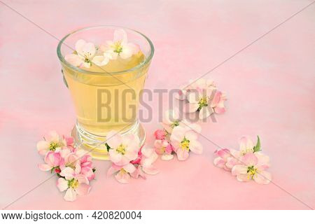 Natural remedy for skincare with apple blossom flowers with hot drink in a glass on pink marble. Can clear acne, provide a clear complexion and help with other skin problems. High in antioxidants.