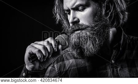 Male Attends Karaoke. Man With A Beard Holding A Microphone And Singing. Man Singing With Microphone