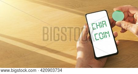 Male Hand With Chia Coin Inscription On Mobile Phone Screen With Green Money In Hand. Eco Sustainabl