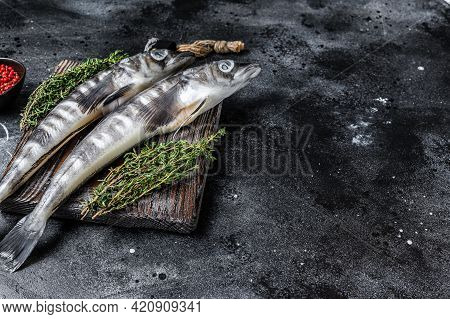 Raw Icefish On A Wooden Cutting Board. Black Background. Top View. Copy Space.