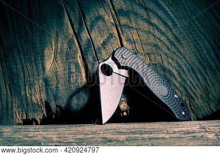 Folding Pocket Knife On A Textured Wood Background. The Knife Is In A Semi-folded Position. Front Vi