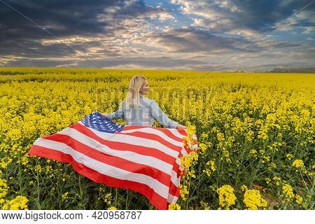 Adult Woman Holding American Flag With Pole, Stars And Stripe In A Yellow Rapeseed Field. Usa Flag F