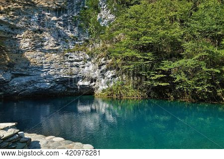 The Calm Turquoise Lake Is Surrounded By Cliffs With Green Vegetation. Reflection On The Surface Of 