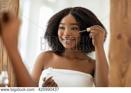 Beauty Cosmetics For Young Skin. Sensual Black Woman Applying Regenerating Serum Onto Her Face Near 