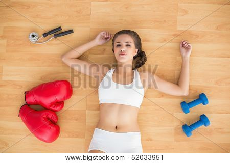 Sporty brunette lying next to jump rope red boxing gloves and dumbbells on the floor
