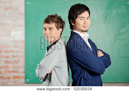 Side view portrait of confident young students standing arms crossed against greenboard in classroom