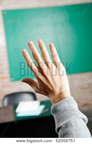 Cropped image of student's hand against greenboard in classroom