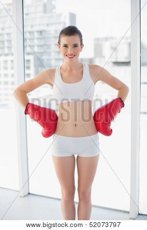 Content fit brown haired model in sportswear wearing boxing gloves in bright fitness studio