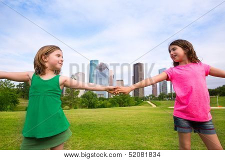 Two sister girls friends playing holding hand in urban modern skyline on park lawn