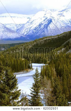 Landscape of high snowy mountains with evegreen trees and frozen river