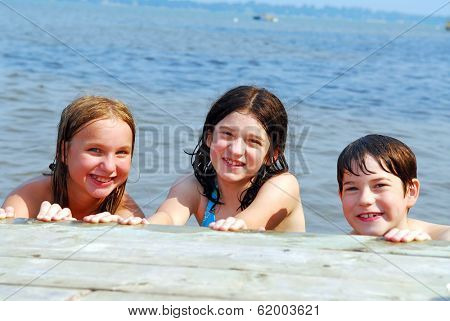Portrait of three children holding onto wooden dock at the lake