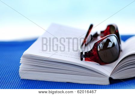 Sunglasses and open book on beach chair - summer vacation concept