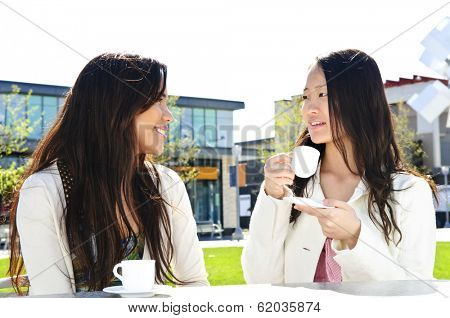 Two girl friends sitting and having drinks at outdoor mall