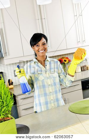 Smiling young black woman with sponge and rubber gloves cleaning kitchen