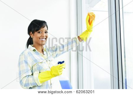 Smiling black woman cleaning windows with glass cleaner