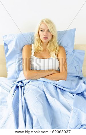 Upset blonde woman sitting in bed with arms crossed