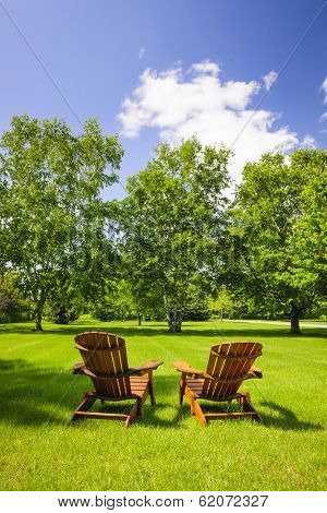 Two wooden adirondack chairs on lush green lawn with trees