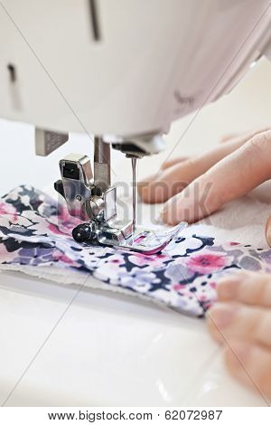 Closeup of hands guiding fabric through sewing machine needle and thread
