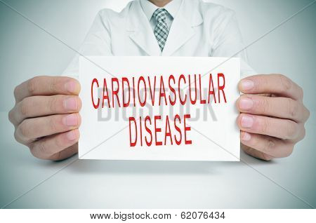 a man wearing a white coat sitting in a desk holding a signboard with the text cardiovascular disease written in it