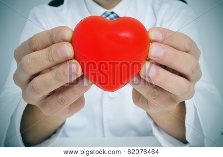 a man wearing a white coat sitting in a desk showing a red heart