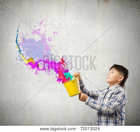 Young boy splashing colorful paint from bucket