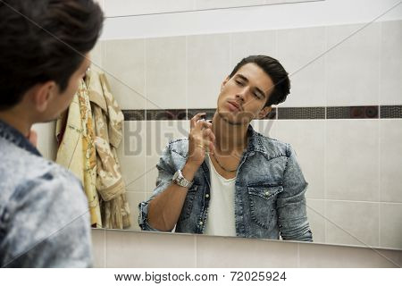 Handsome young man in bathroom, spraying cologne or perfume