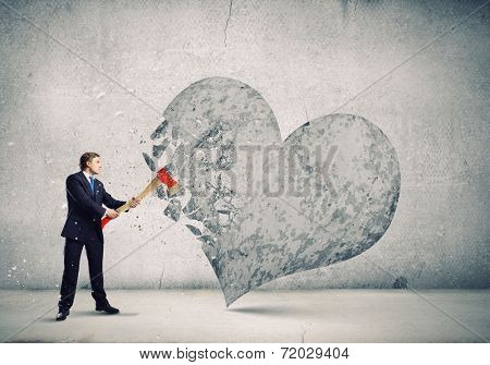 Young determined businessman crashing stone heart with axe