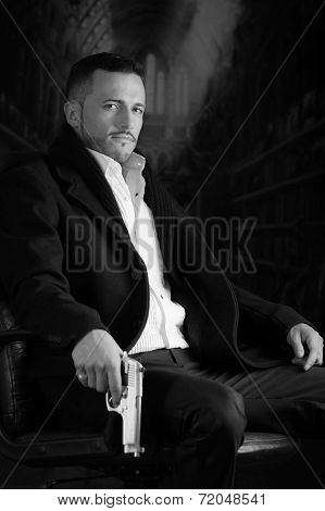 Elegant man sitting in a chair holding  gun over dark background