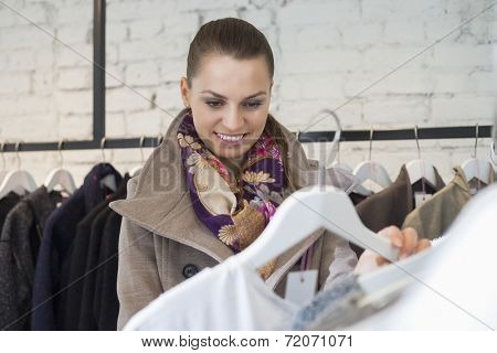 Smiling young woman choosing sweater in store