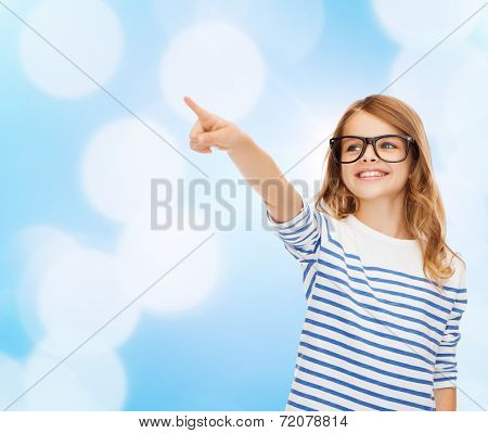 education, school and imaginary screen concept - cute little girl in eyeglasses pointing in the air or imaginary screen