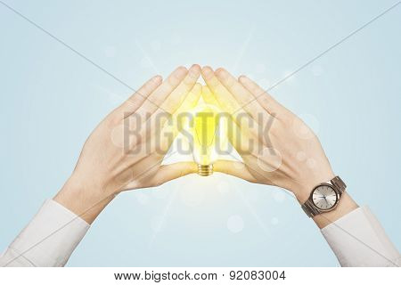Hands creating a form with yellow light bulb in the center
