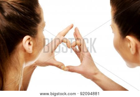 Two beautiful women making heart with fingers.