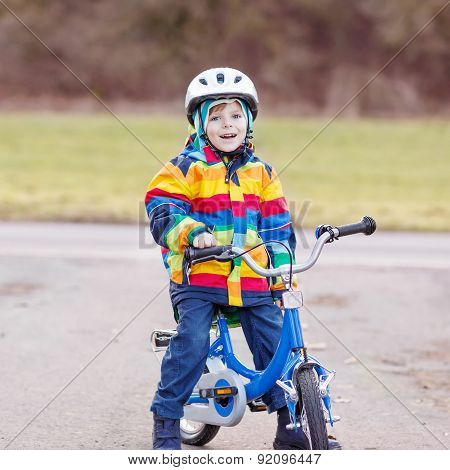 Kid Boy In Safety Helmet And Colorful Raincoat Riding Bike, Outdoors.