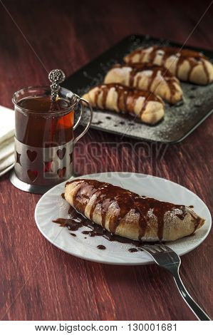 Tasty puff with chocolate glaze on white plate and cup of tea. Selective focus.