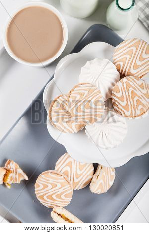 Cookies on white and gray plate with cups of coffee and bottles of milk on white shutters background top view