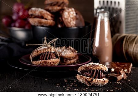 Italian maroni cookies on the plate and bowl with grapes chocolate milkshakes cloth notebook on dark old wooden background