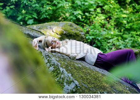 beautiful young girl resting in a forest on the rock