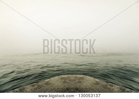 Stone pier in thick fog mystic. Toned image.