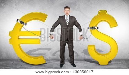 Man chained with golden dollar and euro signs on grey bckground
