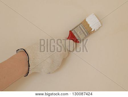 hand with brush in white paint near the wall