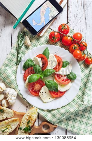 Italian traditional salsd caprese and traveler smartphone with Italy map