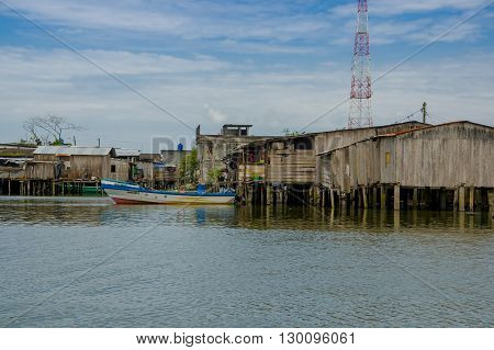 Muisne, Ecuador - March 16, 2016: Muisne waterfront homes as seen from water, modest concrete houses sitting on poles, pacific ocean, fishing boat tied to pier and beautiful blue sky.