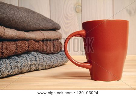 Pile of knitted sweaters and a cup on a wooden background