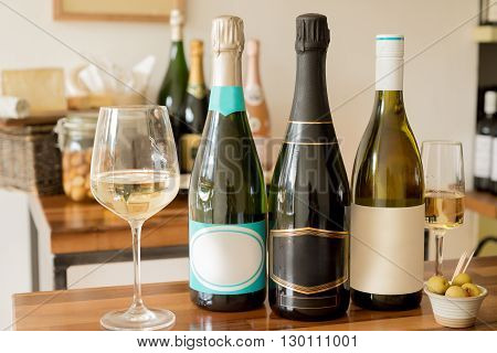 Bottles of unopened champagne or sparkling wine with blank labels between wineglasses and a tiny bowl of olives