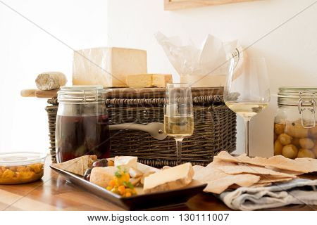 Two glasses of wine with servings of cheese and biscuits alongside a jar of honer, olives, and a wicker basket.