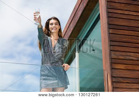 Low angle view of gorgeuos woman showing champagne flute while standing by glass railing at balcony